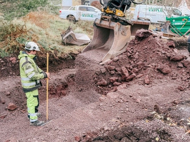 Mann med spade foran gravemaskin