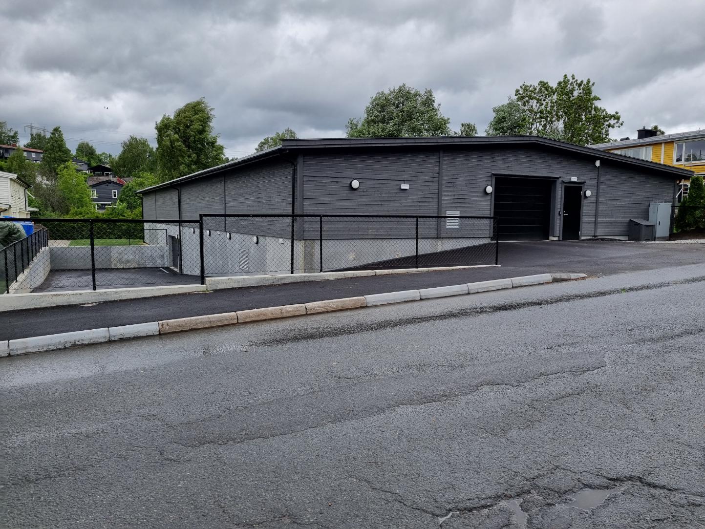 Mørkt næringsbygg med asfaltert uteområde og inngjerdet nedkjøring