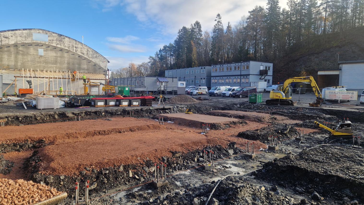 Grunnarbeid på byggeplass med gravemaskin og brakker